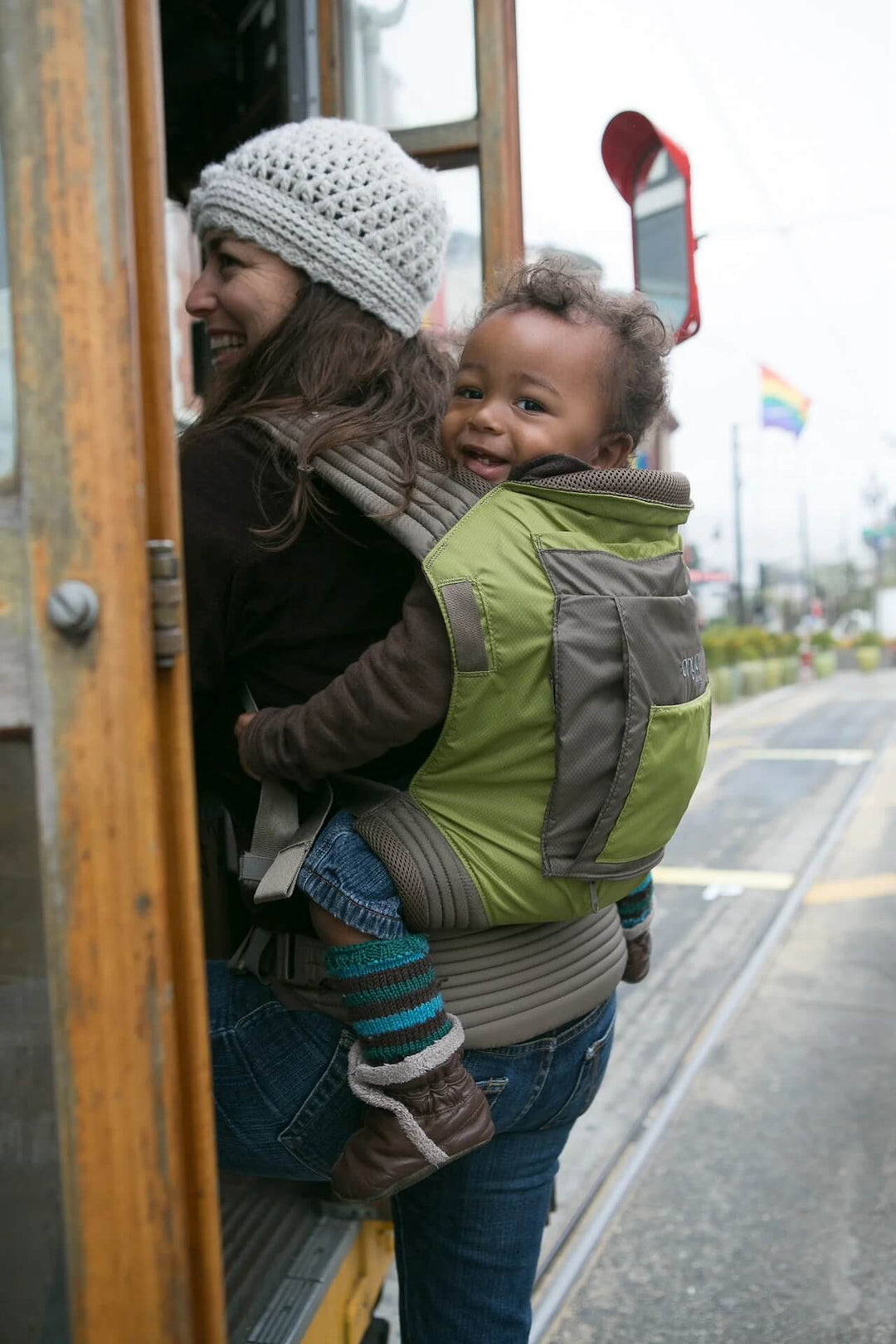 Woman boarding a bus with smiling baby in an Onya Baby Outback in the back carry position