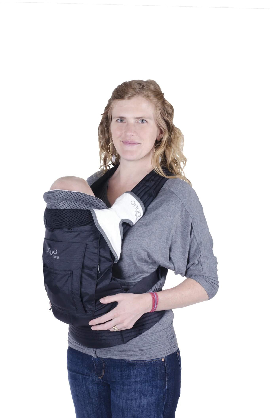 Smiling woman standing and carrying infant in an Onya Baby Outback in the front carry position using a Baby Booster Infant Insert