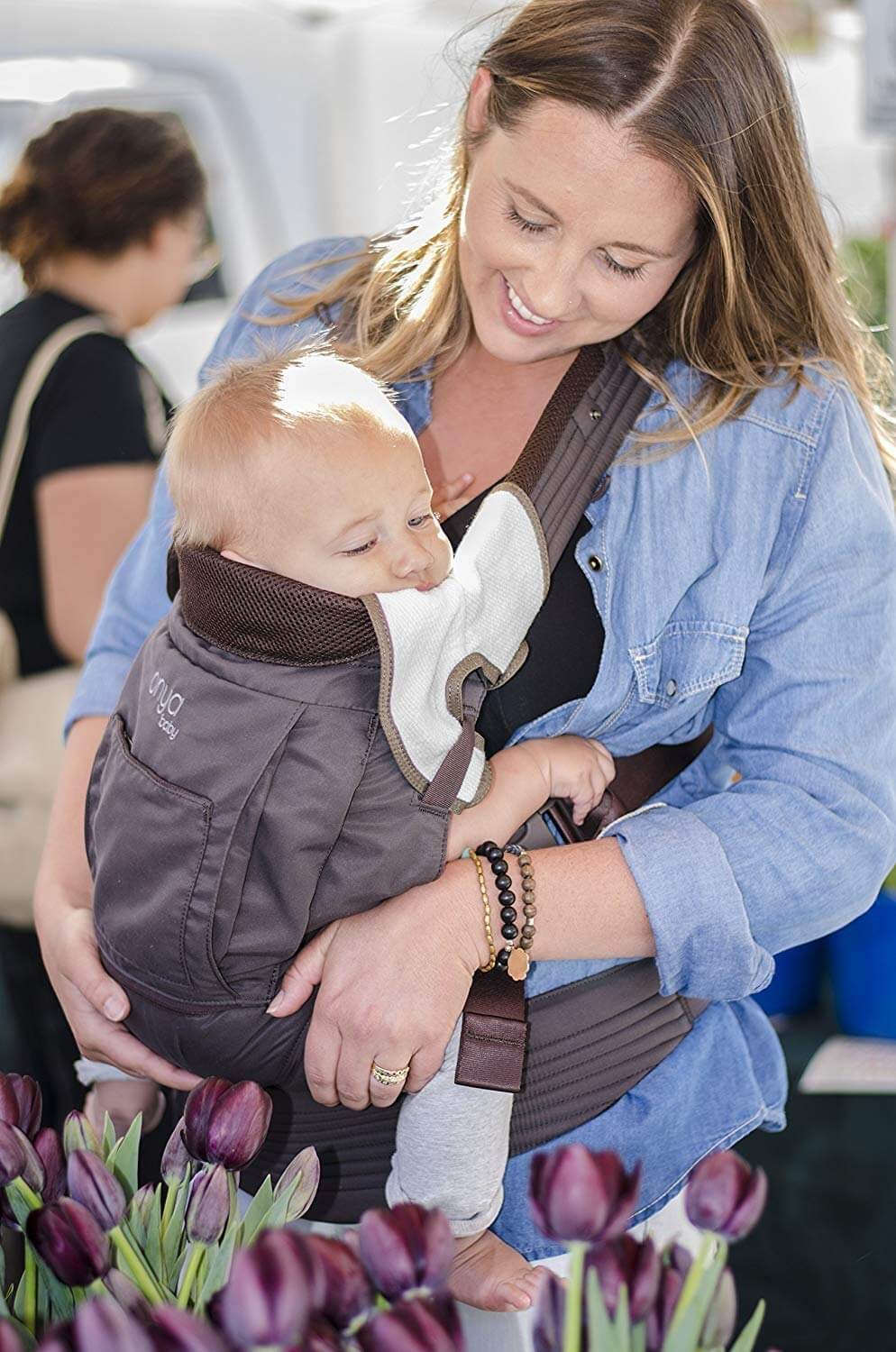 Woman carrying baby in an Onya Baby Nexstep in the front carry position while baby bites on teething pad