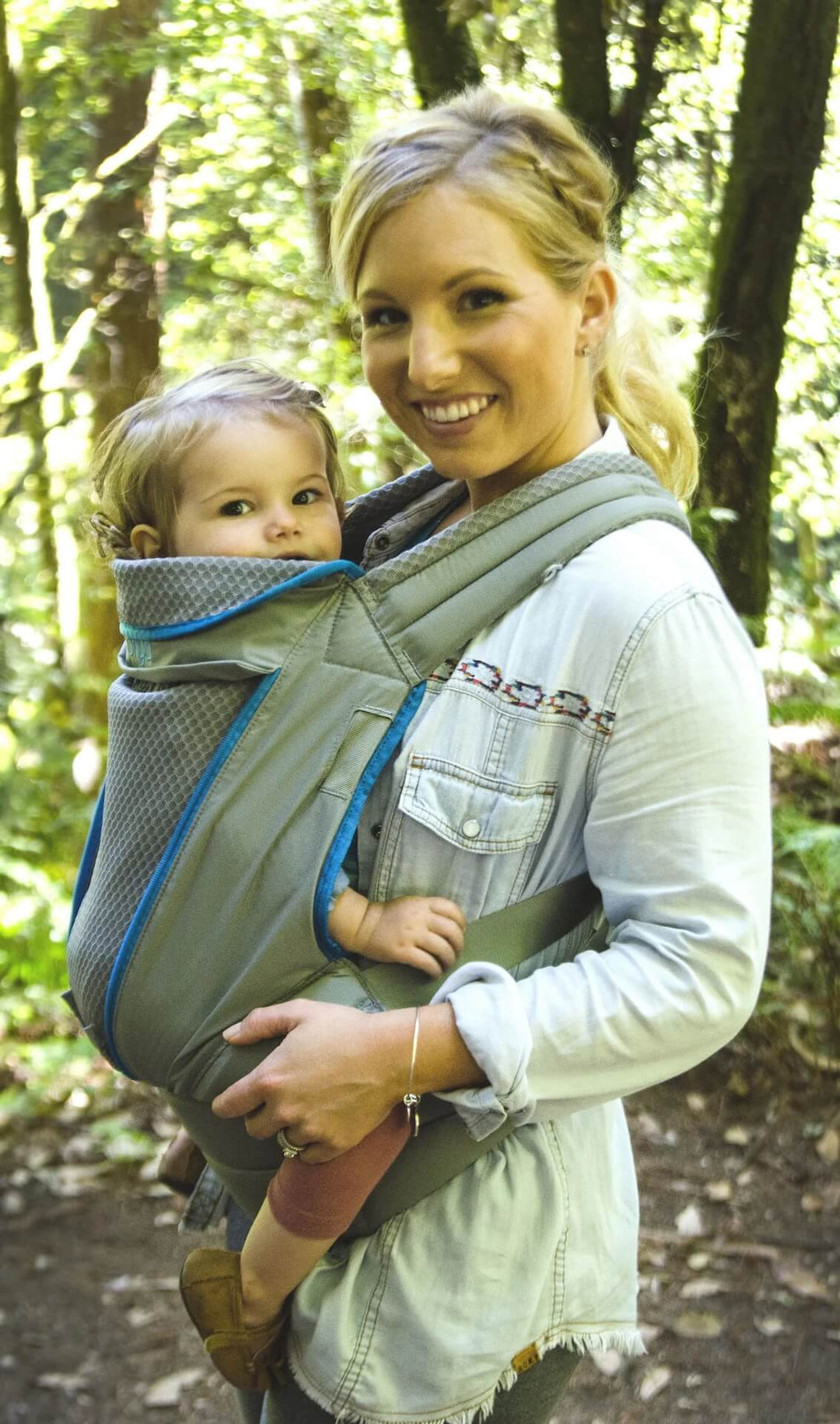 Smiling woman standing on a forest trail with baby in an Onya Baby Pure in the front carry position