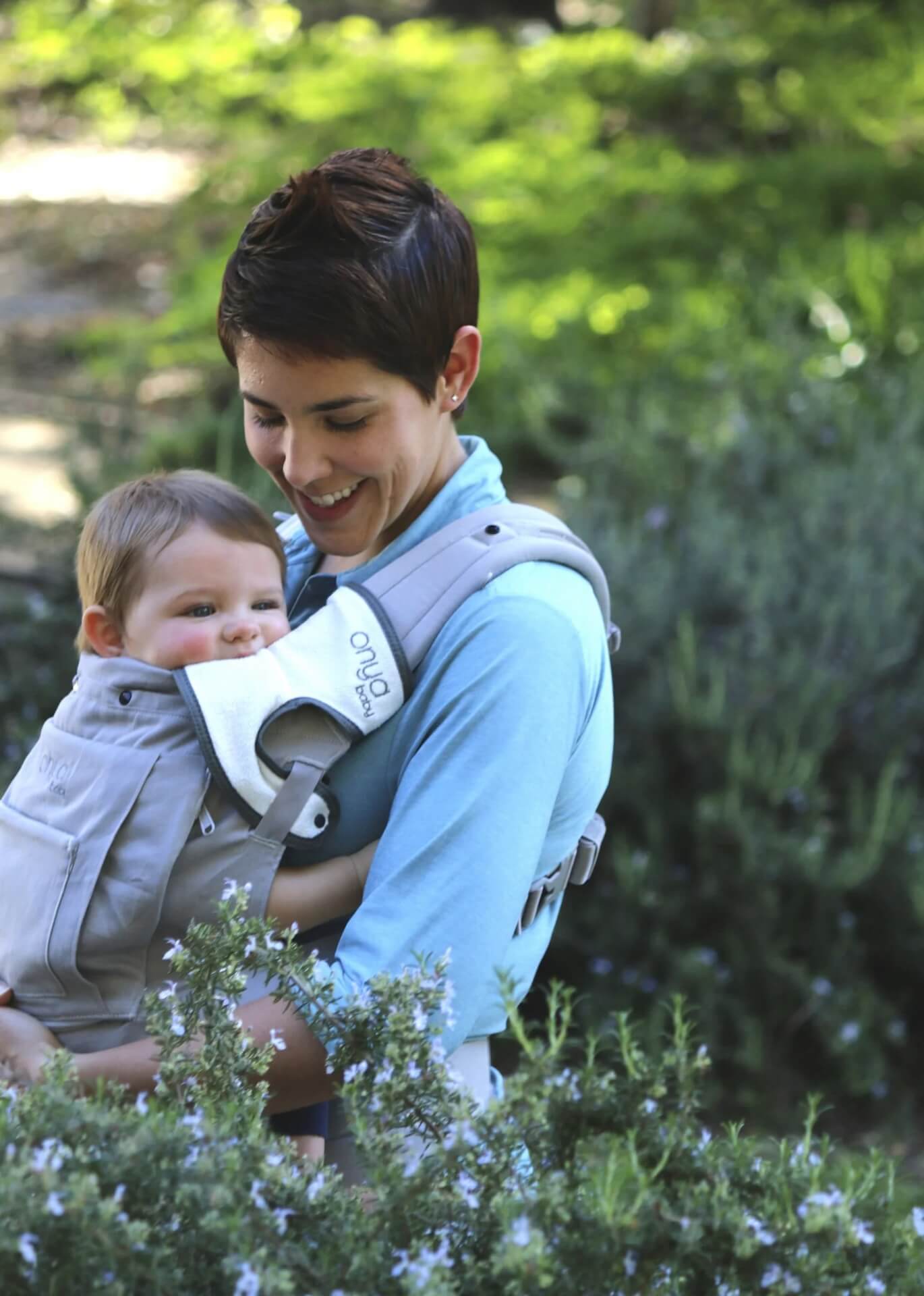 Woman carrying baby in an Onya Baby Cruiser in the front carry position while baby bites on teething pad