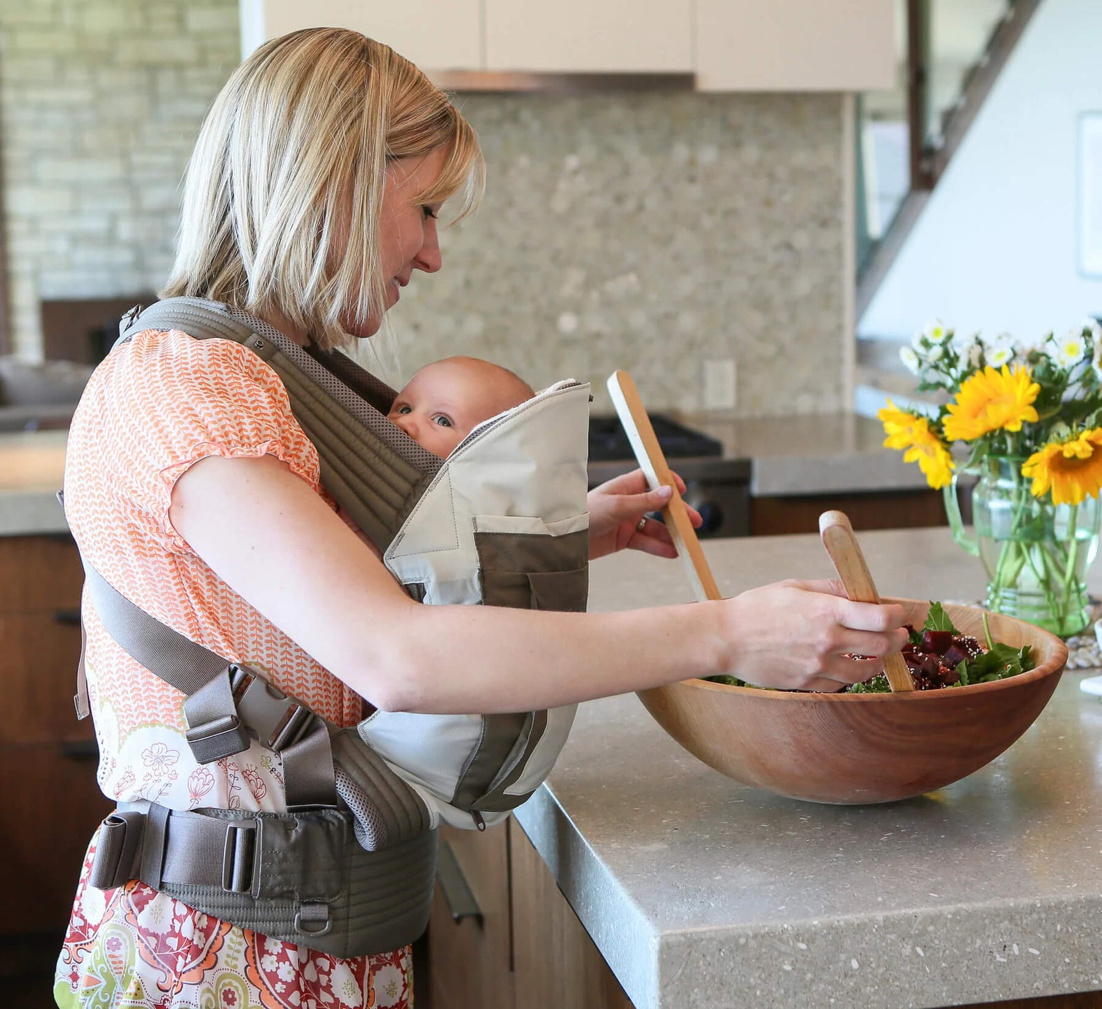 Woman making a salad while carrying infant in an Onya Baby Outback in the front carry position using a Baby Booster Infant Insert