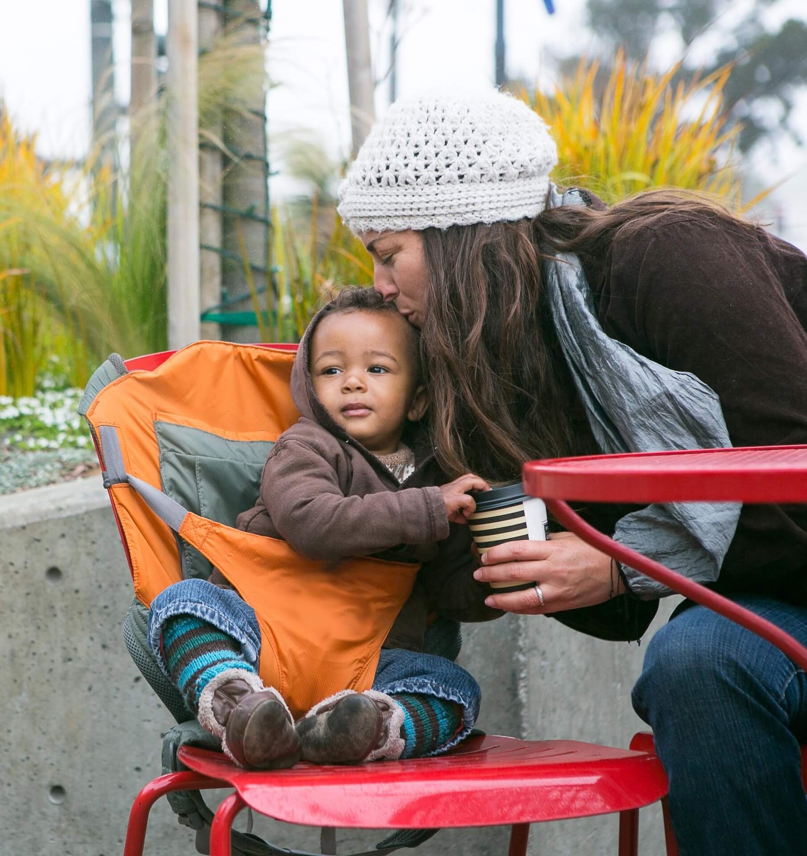 Woman sitting and leaning over to kiss baby sitting in an Onya Baby Outback converted to chair harness outside of coffee shop