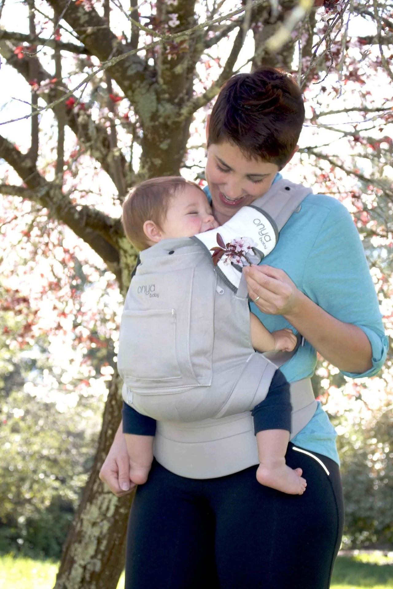 Woman carrying baby in an Onya Baby Cruiser in the front carry position while baby bites on teething pad