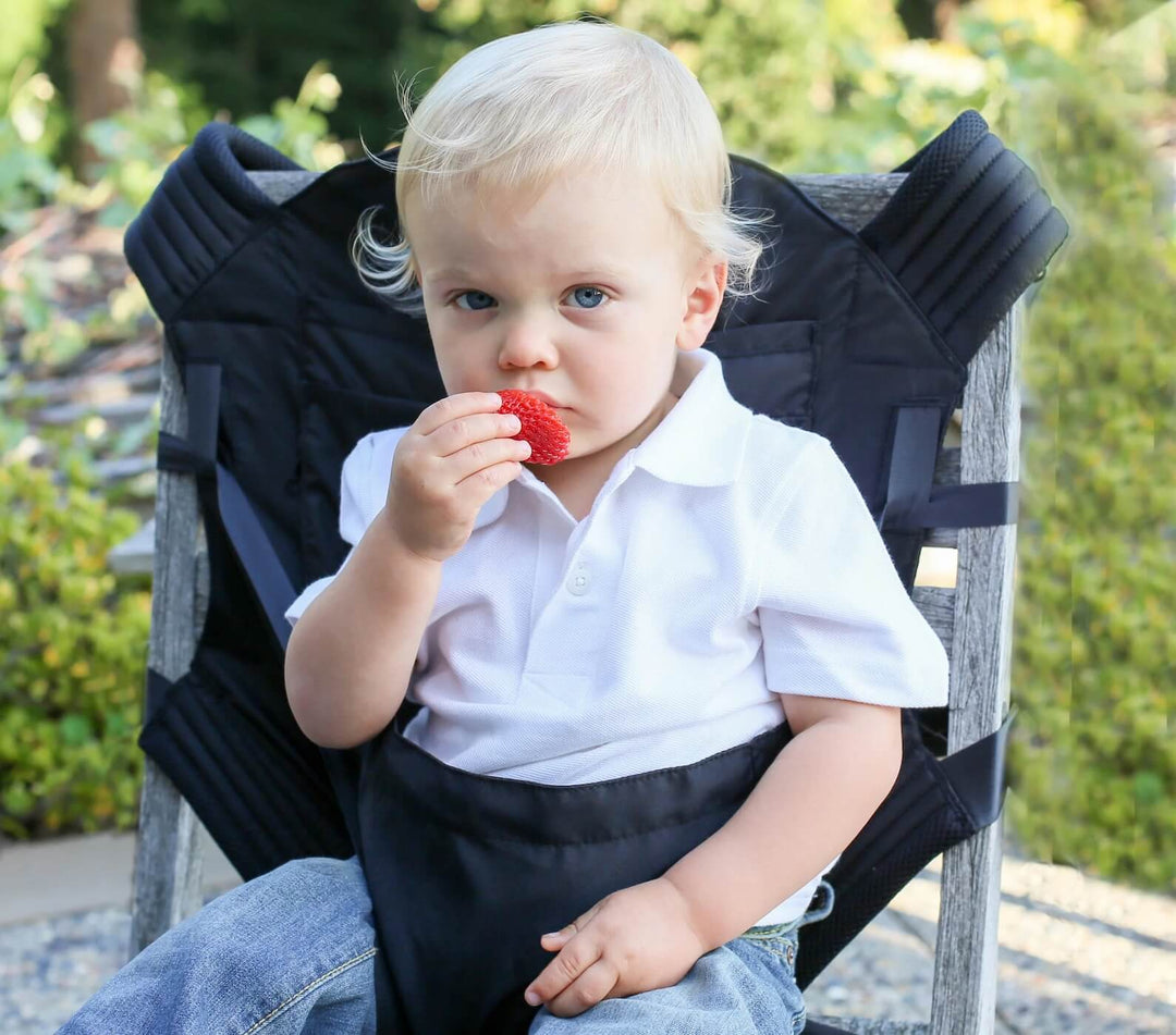 Baby looking at the camera while eating a strawberry in an Onya Baby Outback carrier converted into chair harness