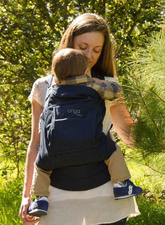 Woman carrying baby in an Onya Baby Cruiser in the front carry position while walking on a forest trail
