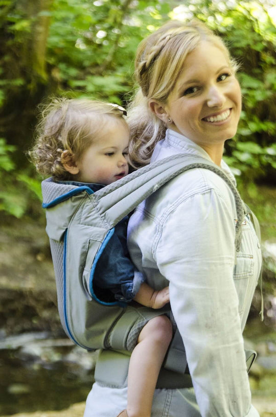 Smiling woman standing on a forest trail with baby in an Onya Baby Pure in the back carry position